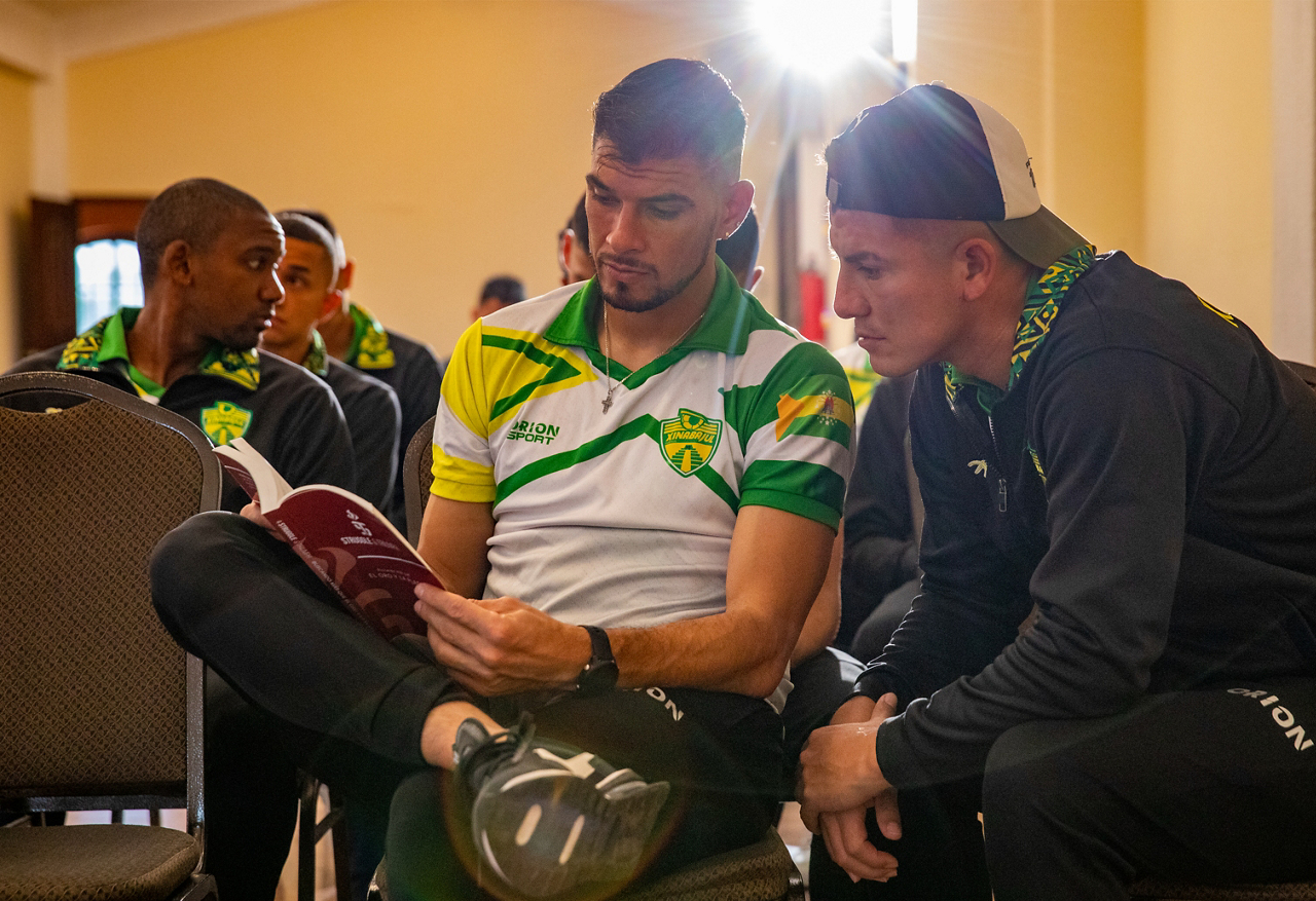 Kristian Guzman (holding book) team captain of the Xinabajul Soccer Club, shows an AIA® Sports Bible to one of his players.