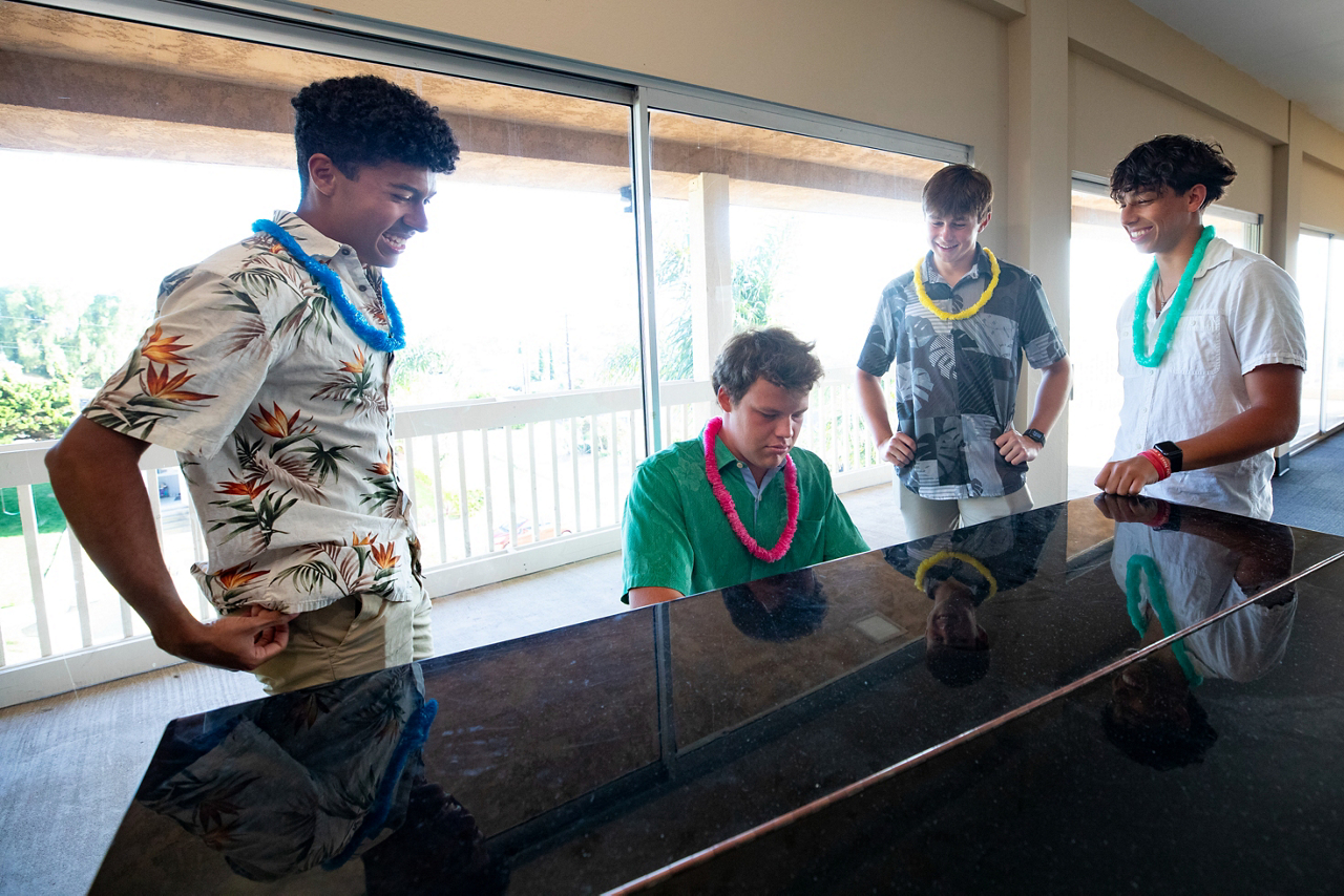 Adam, Logan and Ryan (standing, left to right) watch as Troy plays piano.