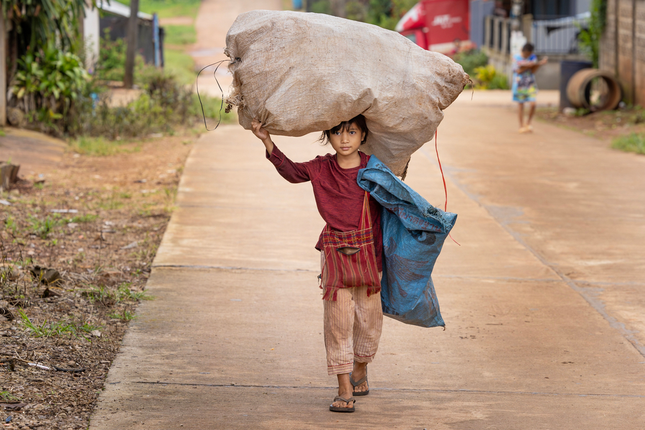 child carrying sack on head walking on a road