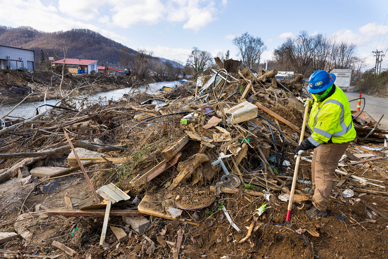Hurricane Helene damage in Swannanoa, NC. Ryan and Amy Geist Cru Lifelines staff  and students rebuilding homes. Worker raking trash alongside Swannanoa river. 