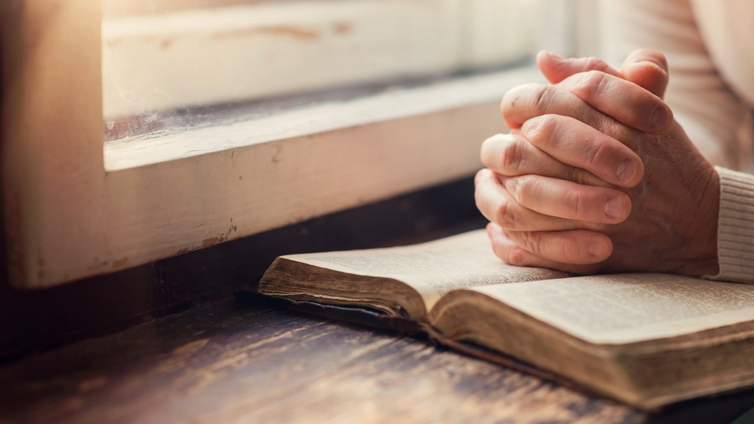 Hands of an unrecognizable woman with Bible praying