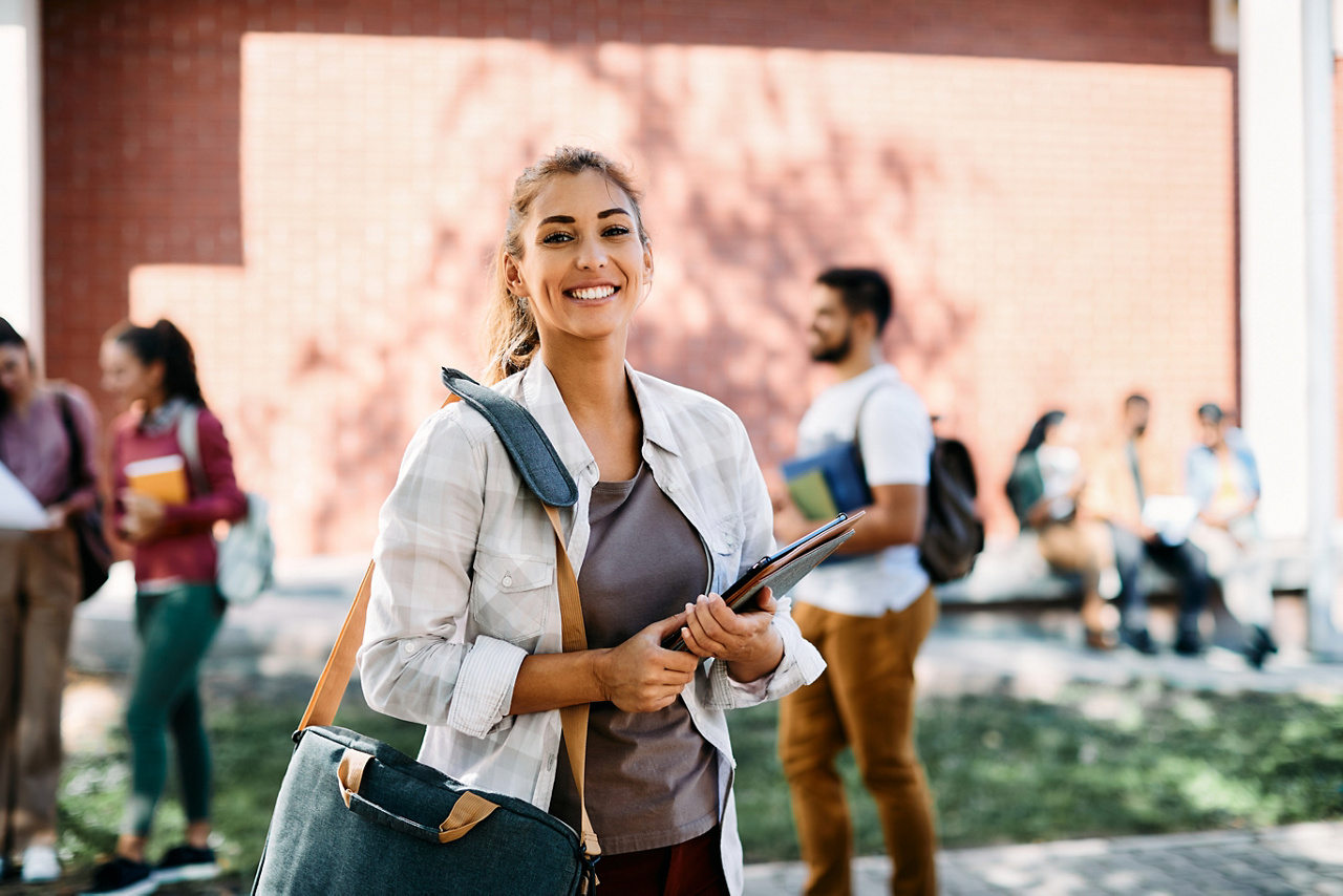 Portrait of happy female student going to lecture at the university and looking at camera.