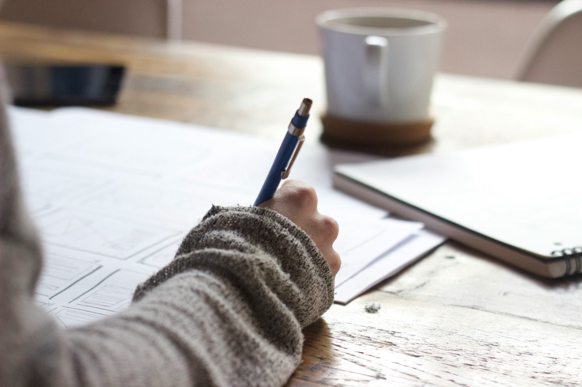 Person writing on paper with a coffee cup in the background