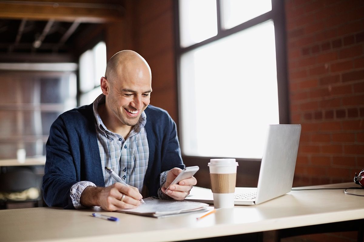 Man smiling sitting at laptop looking at phone