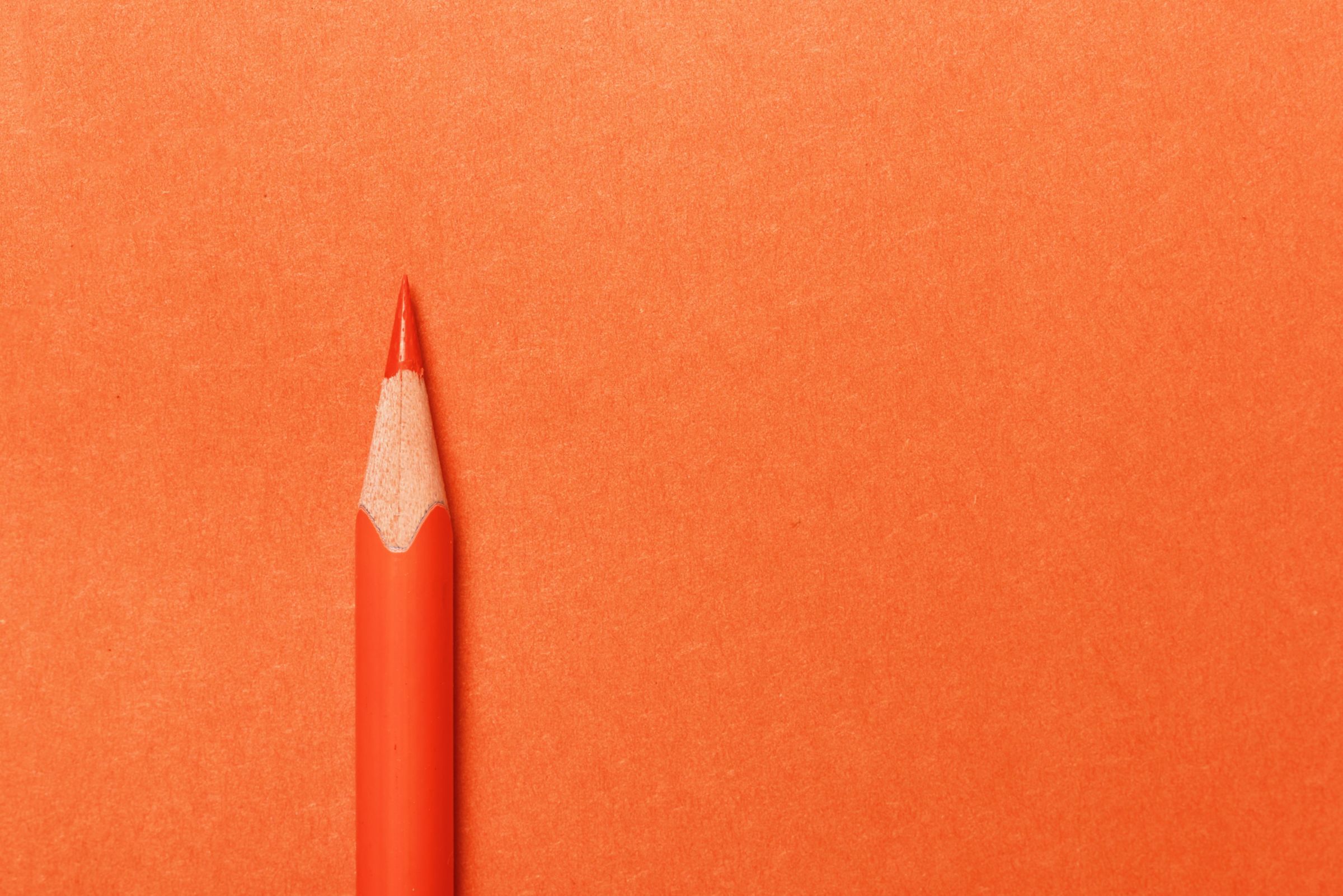 Orange pencil lies on an orange paper background.