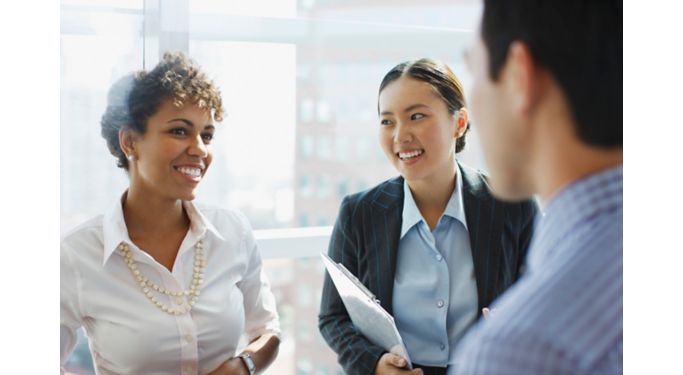 Group of diverse Fiserv Employees in office attire and having a nice conversation, two are female presenting individuals smiling at a male-presenting individual