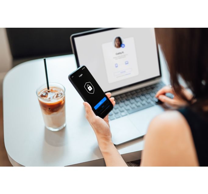 Over the shoulder view of young woman using laptop, logging in online banking account with digital security device at cafe. Internet security and digital privacy protection concept.