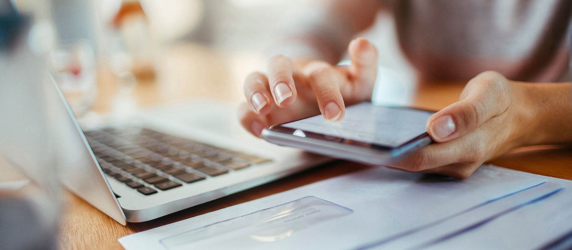 Woman's hand holding phone sitting in front of laptop