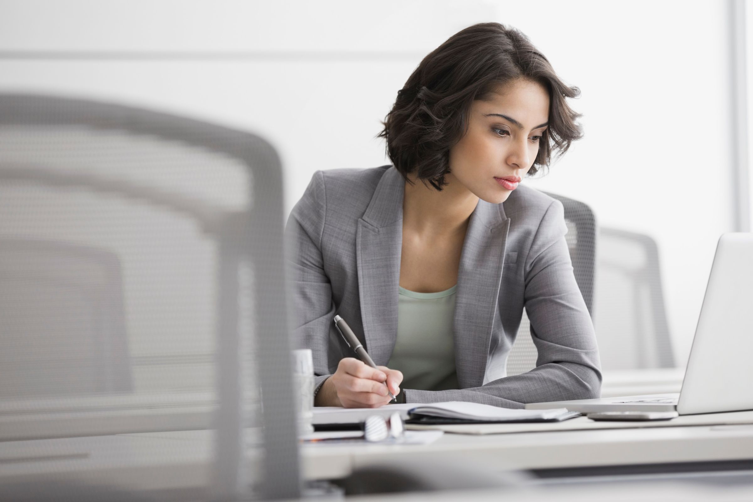 a woman sitting infront of laptop and  writing on a notepad