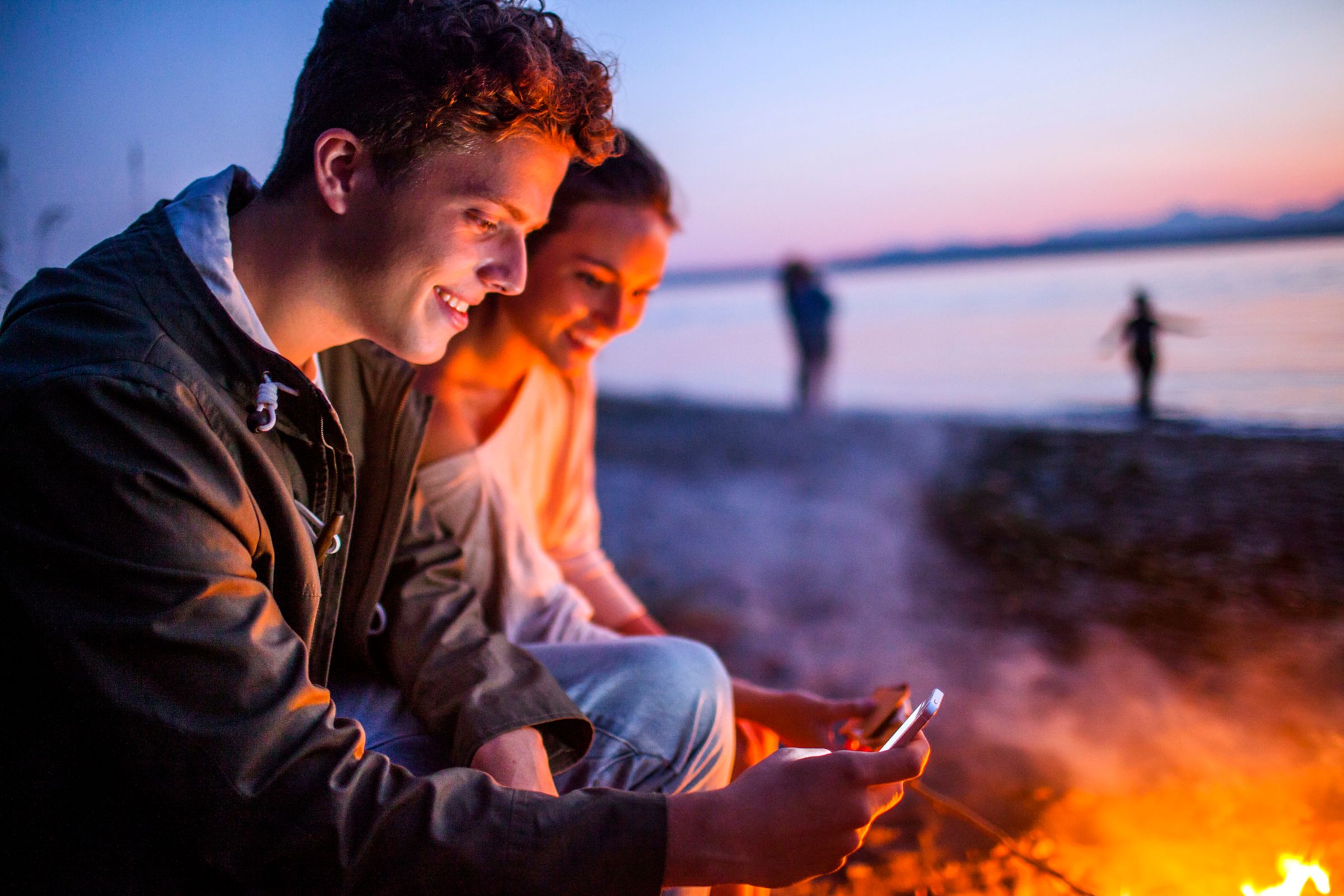 People sitting at a bonfire on the beach.