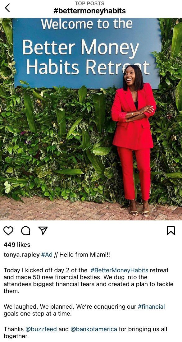 A screenshot of an Instagram post featuring a female-presenting person in a red pantsuit standing in front of a big blue sign with white text that reads: "Welcome to the Better Money Habits Retreat"