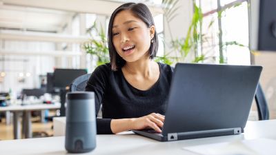Asian woman talking to Alexa and typing on laptop