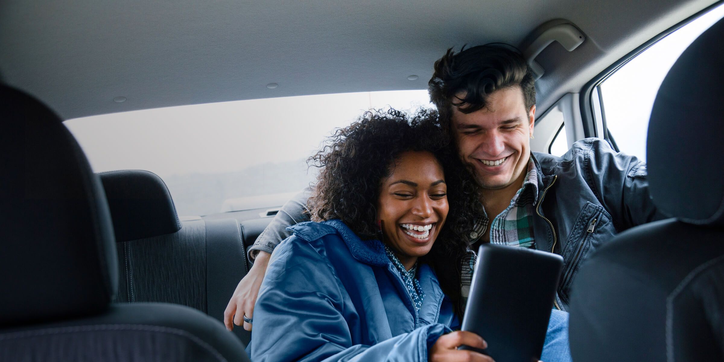 a man and woman happily looking at a tablet in a car