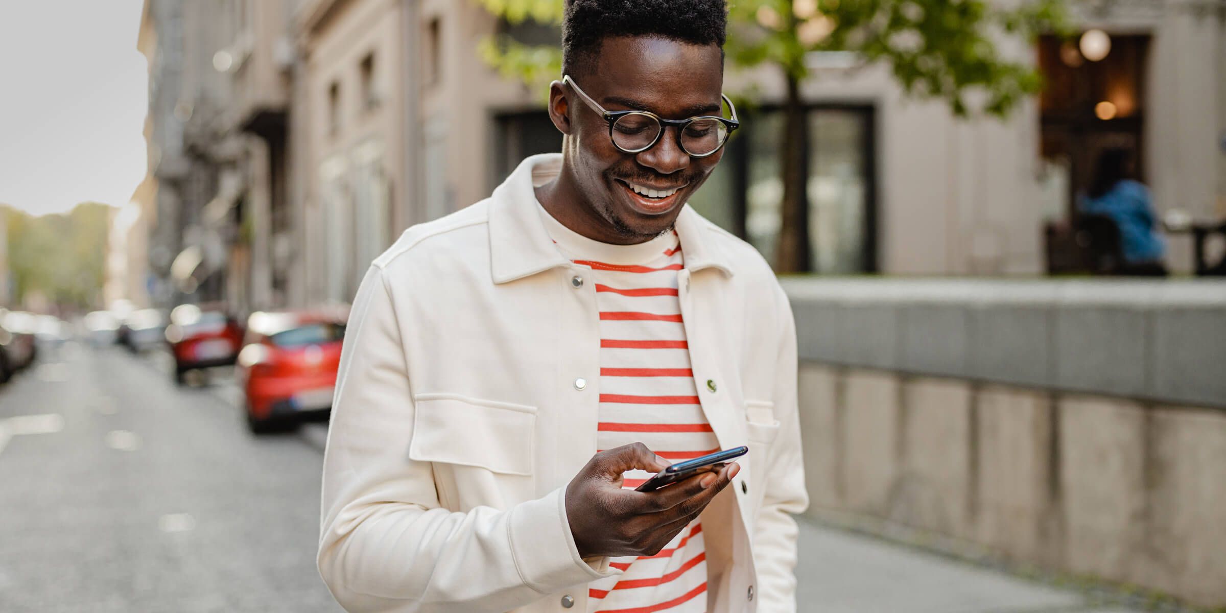 Young black man standing by street holding phone