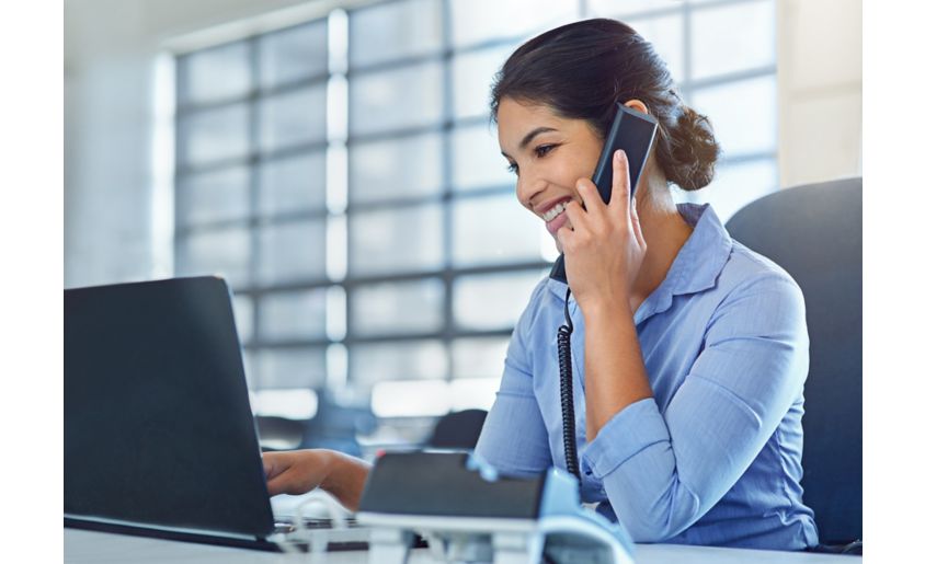 Shot of a young businesswoman talking on the phone while using a laptop at work