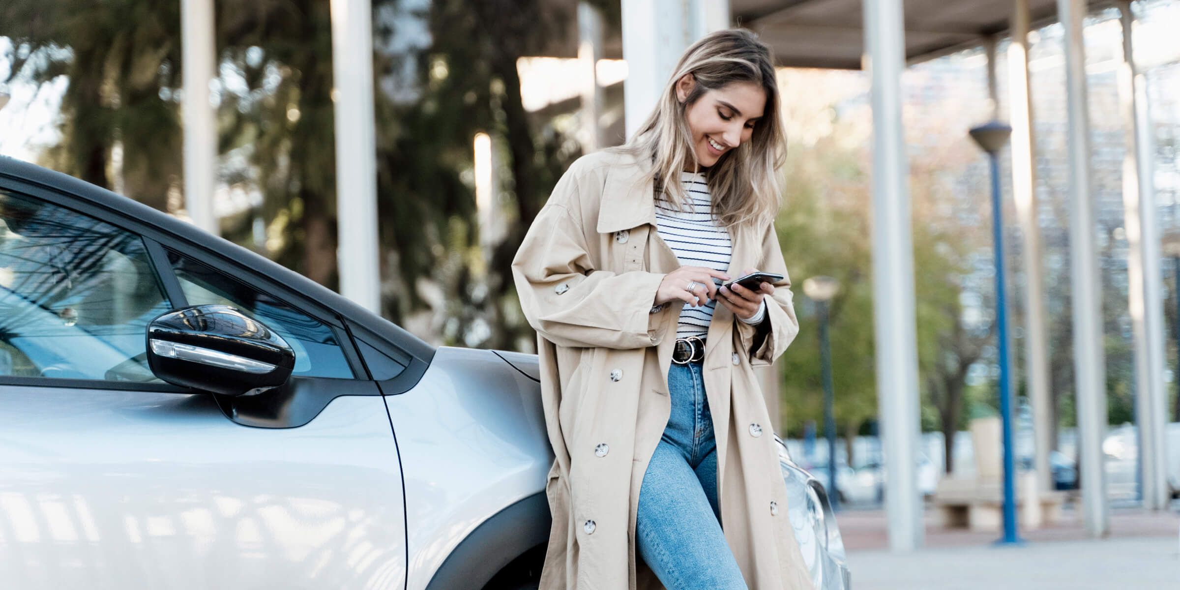 Woman leaning on car smiling and scrolling on phone