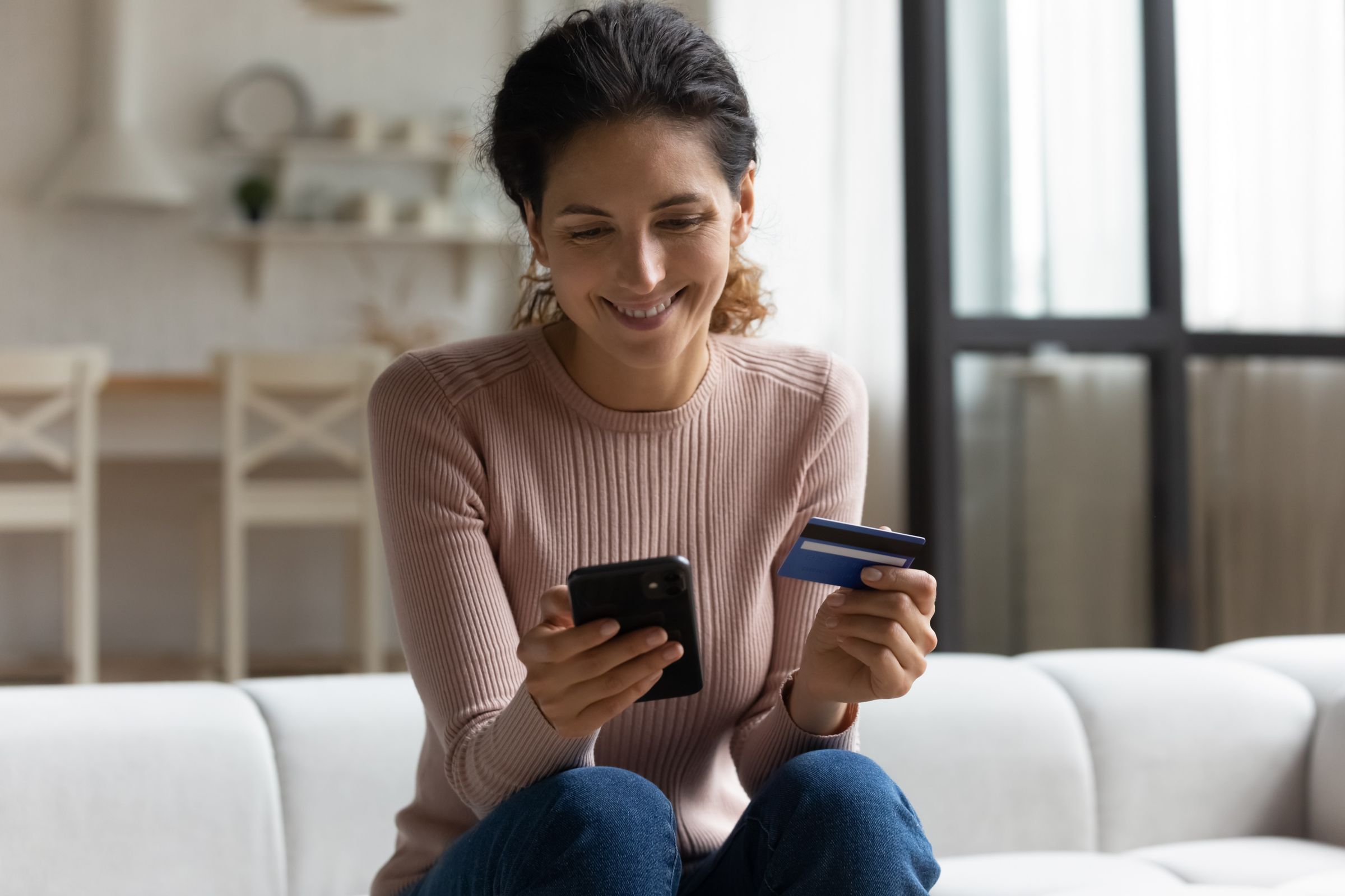 Smiling latina lady client hold mobile phone and credit card for online shopping payment.