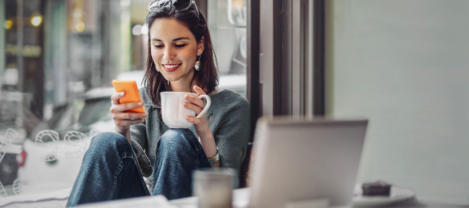 A woman looks at phone with coffee in other hand