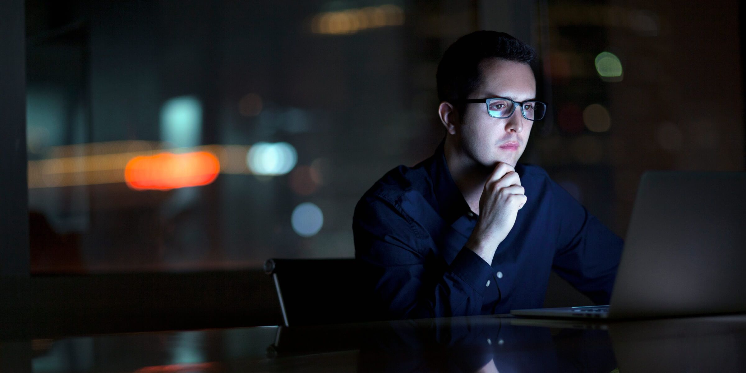 a man sitting and watching a laptop at a table with his hand on his chin