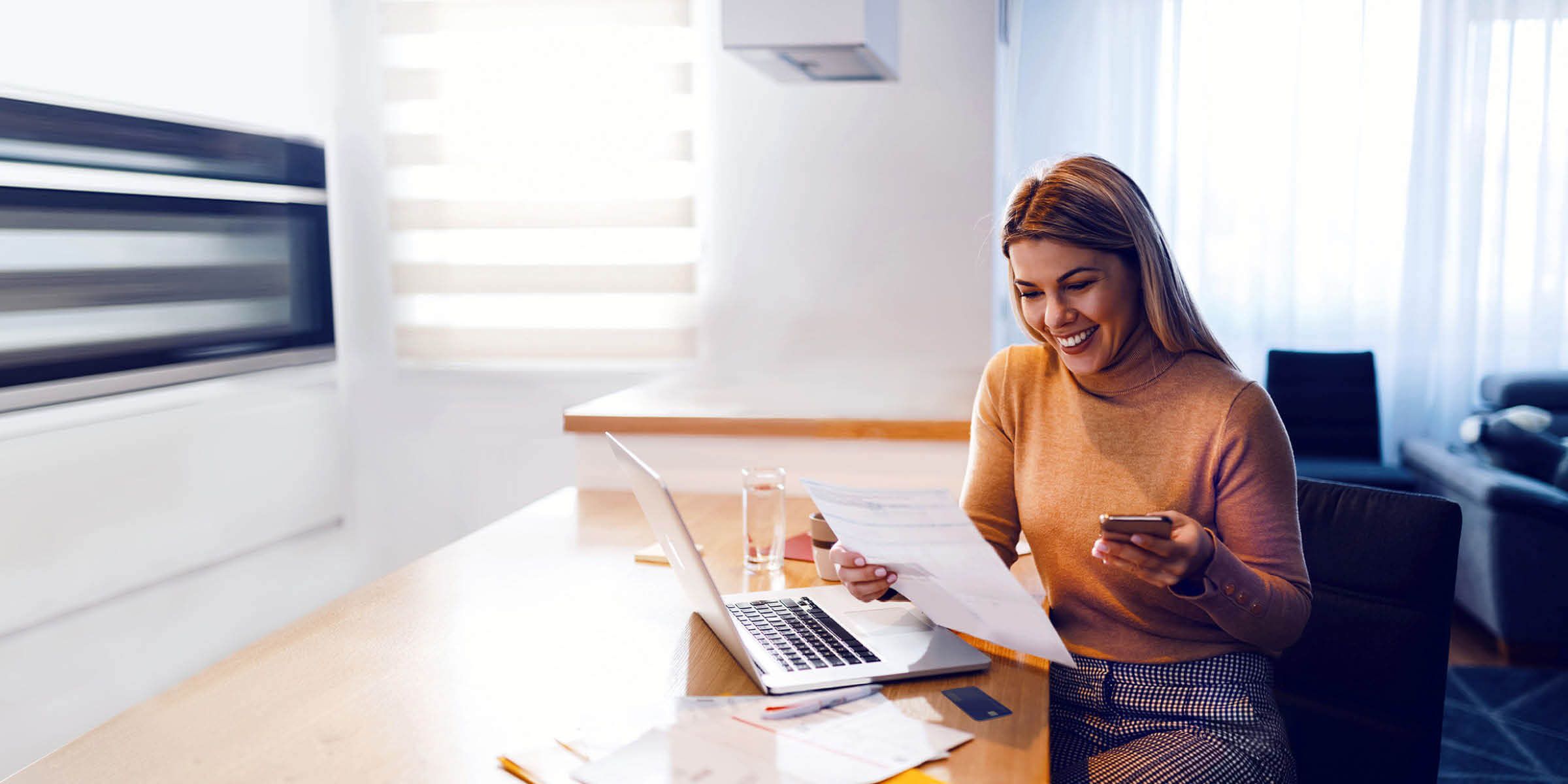 Person sitting at their desk and reviewing paper billing statement with laptop open.