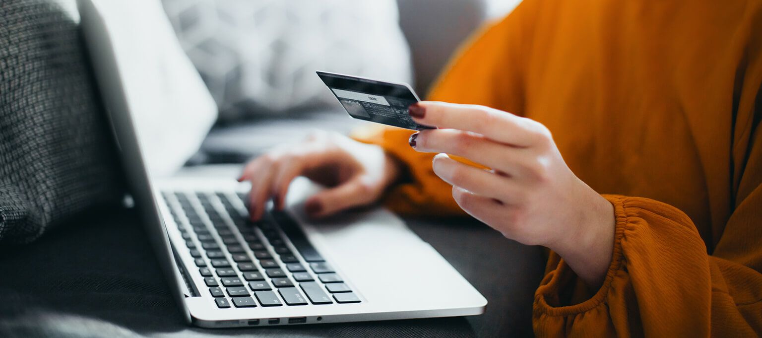 Woman holding card in front of laptop 