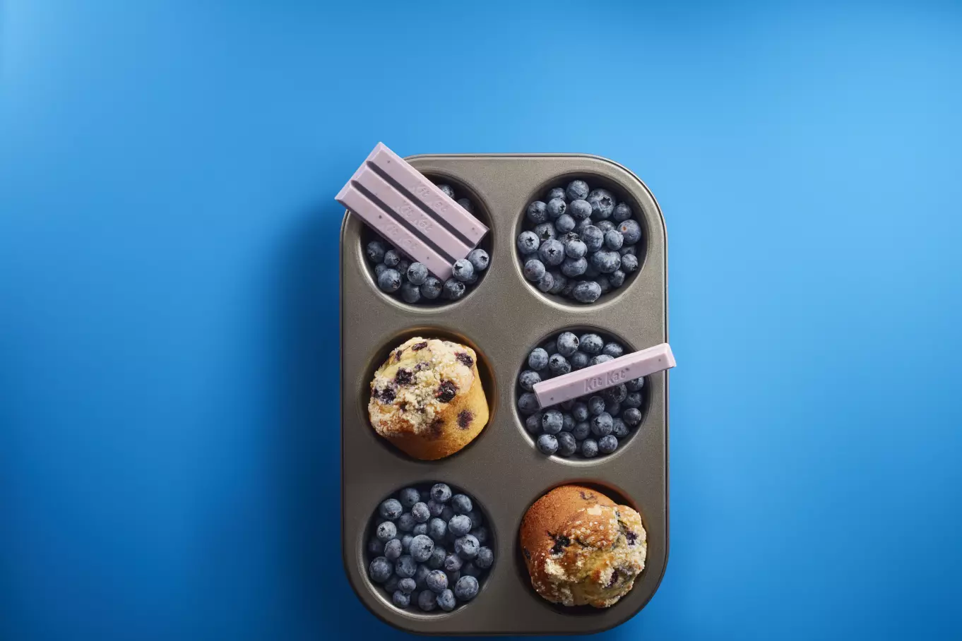 Unwrapped candy bars inside muffin tin with blueberries and muffins