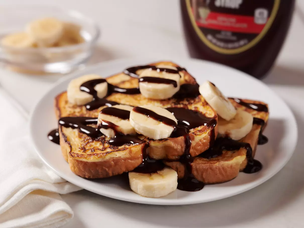 French toast with banana slices and HERSHEY'S SPECIAL DARK Mildly Sweet Chocolate Syrup on top