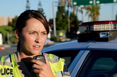 A female police officer standing next to her car about to talk on the radio.; Shutterstock ID 138753710