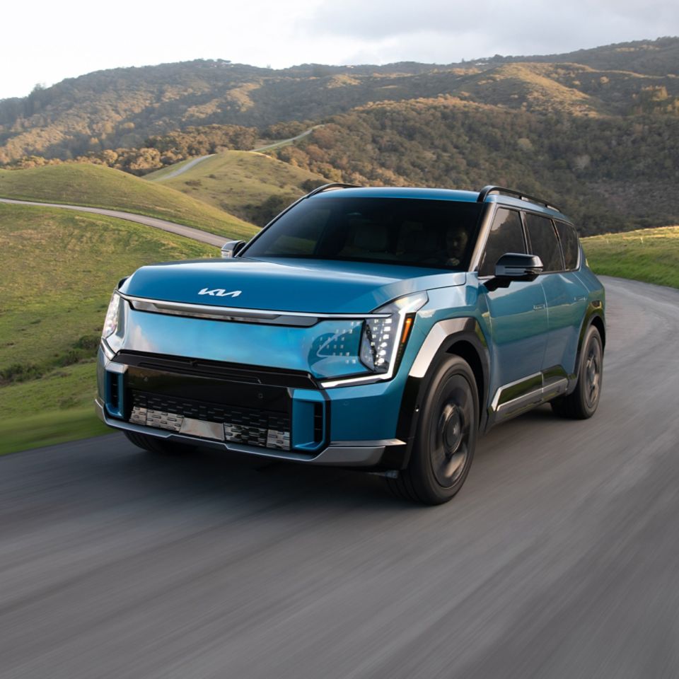 2025 Kia EV9 in blue, three-quarter front view, driving through a paved road