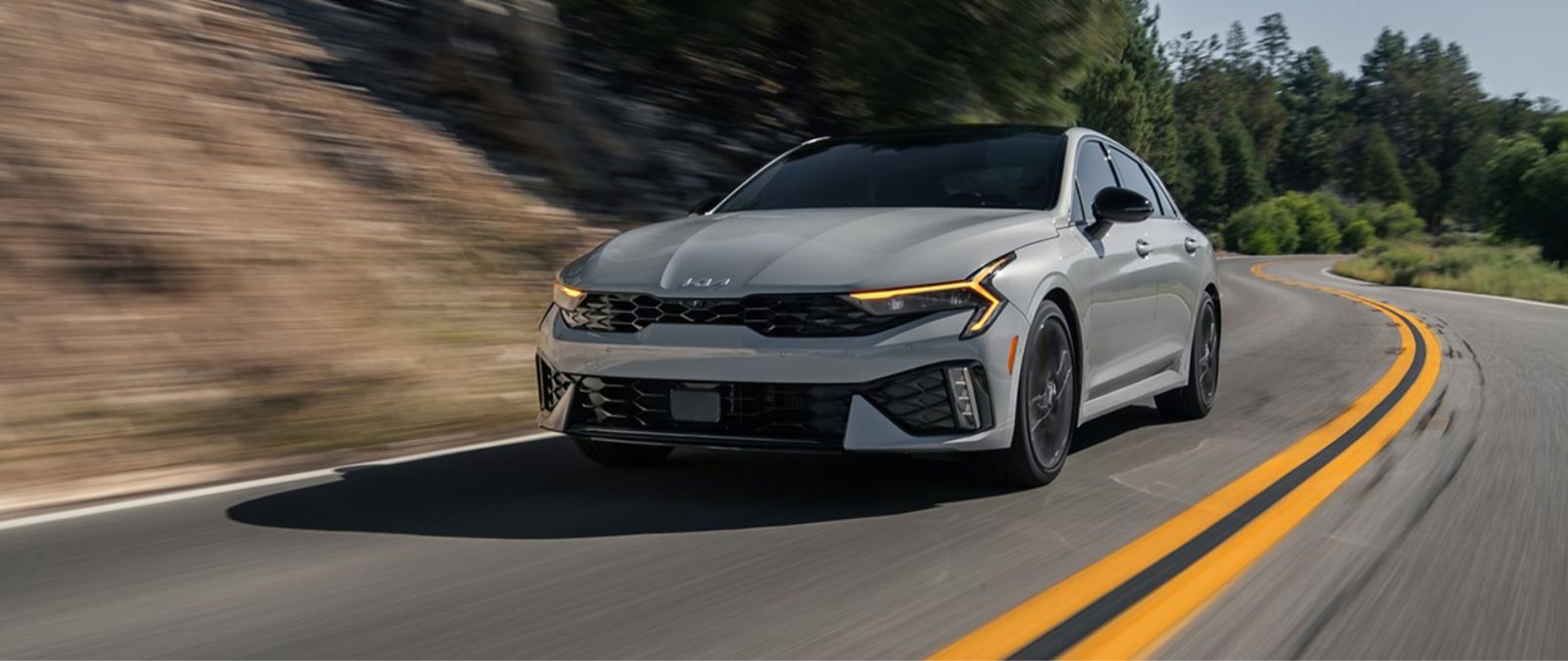 Front driver-side view of the 2025 Kia K5 on a twisting rural road