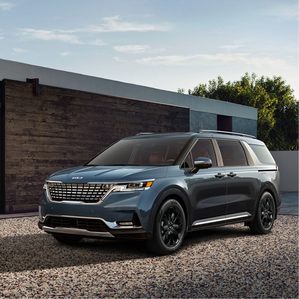 Front driver-side three-quarter view of a blue-green Kia SUV parked in front of a modern wood and cement building.