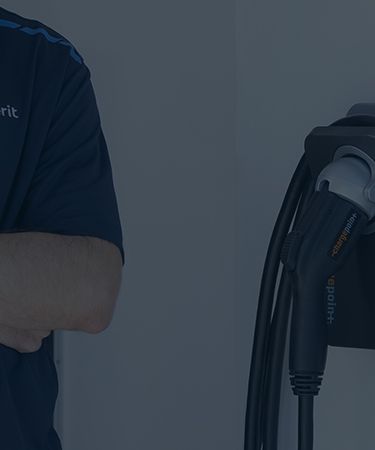 Man with arms folded standing next to EV charger on a wall