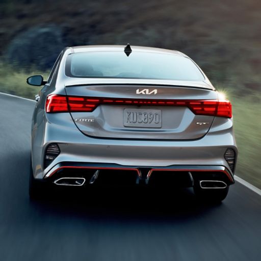2024 Kia Forte in silver, driving through a curve, rear view of taillights and tailpipes