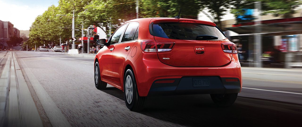 2023 Rio 5-Door in red, rear 3-quarter view driving down a city street