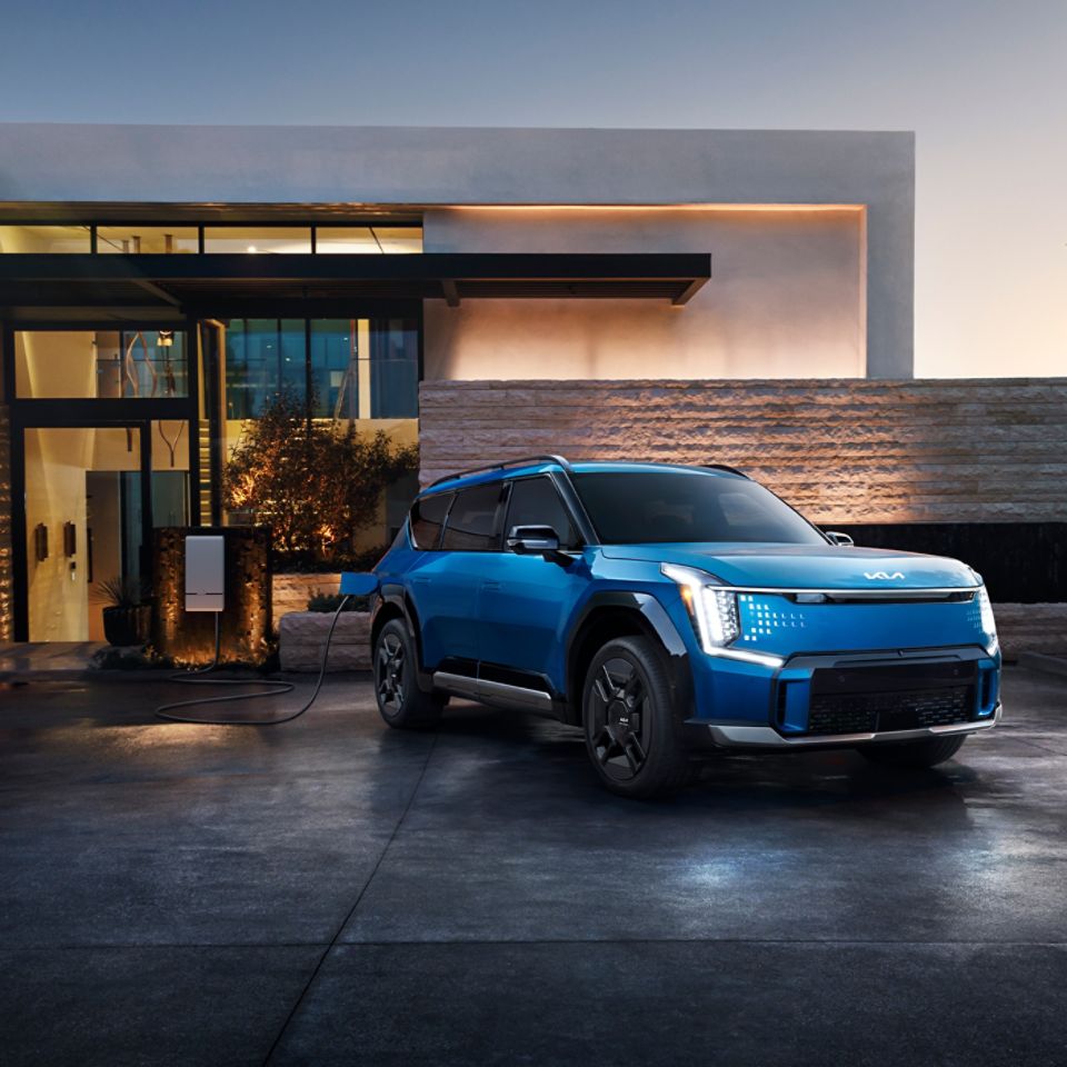 Blue 2026 Kia EV9 being charged in front of a house