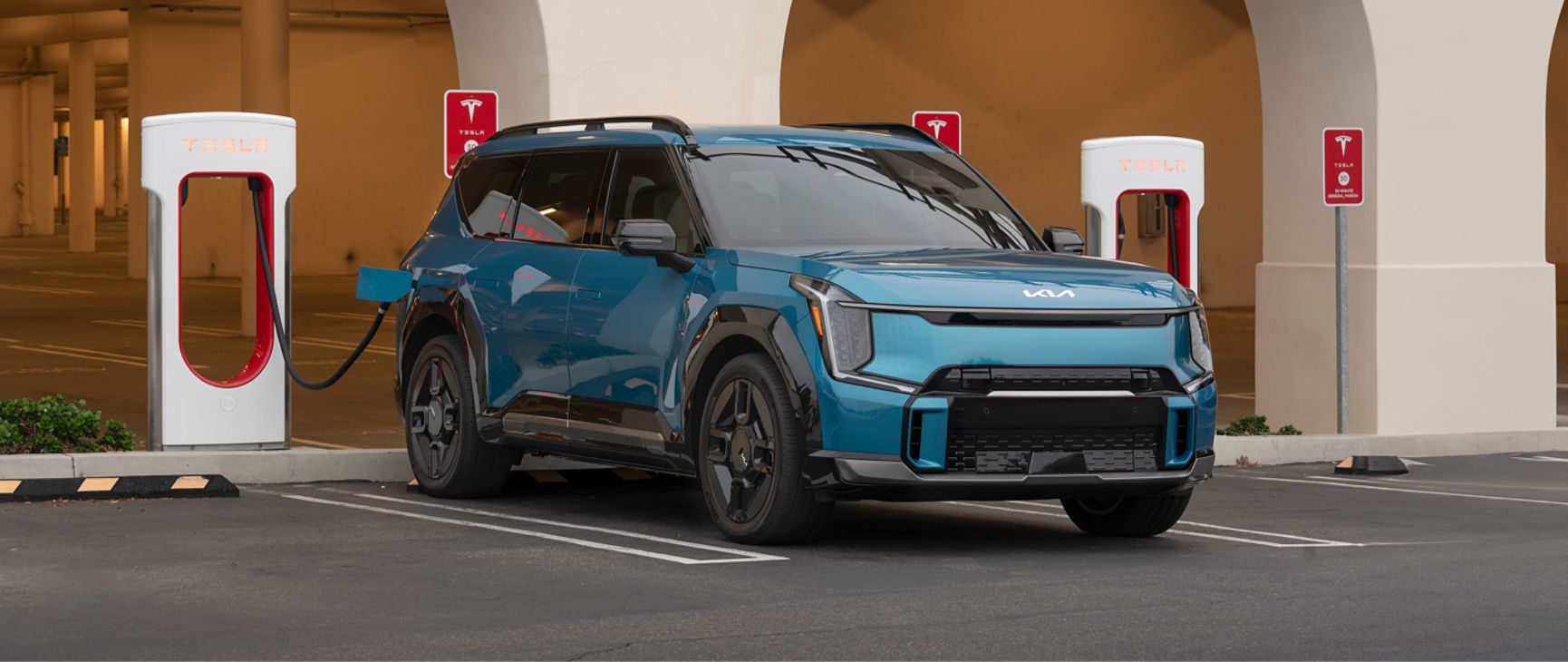 Blue 2026 Kia EV9 being charged at a Tesla Charging station