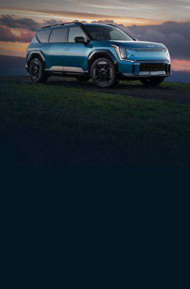 2026 Kia EV9 in blue, three-quarter front view, driving on a winding road