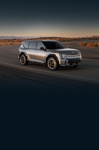 2026 Kia EV9 GT in gray, three-quarter front view, parked on the road in the desert with the star map LED headlights on