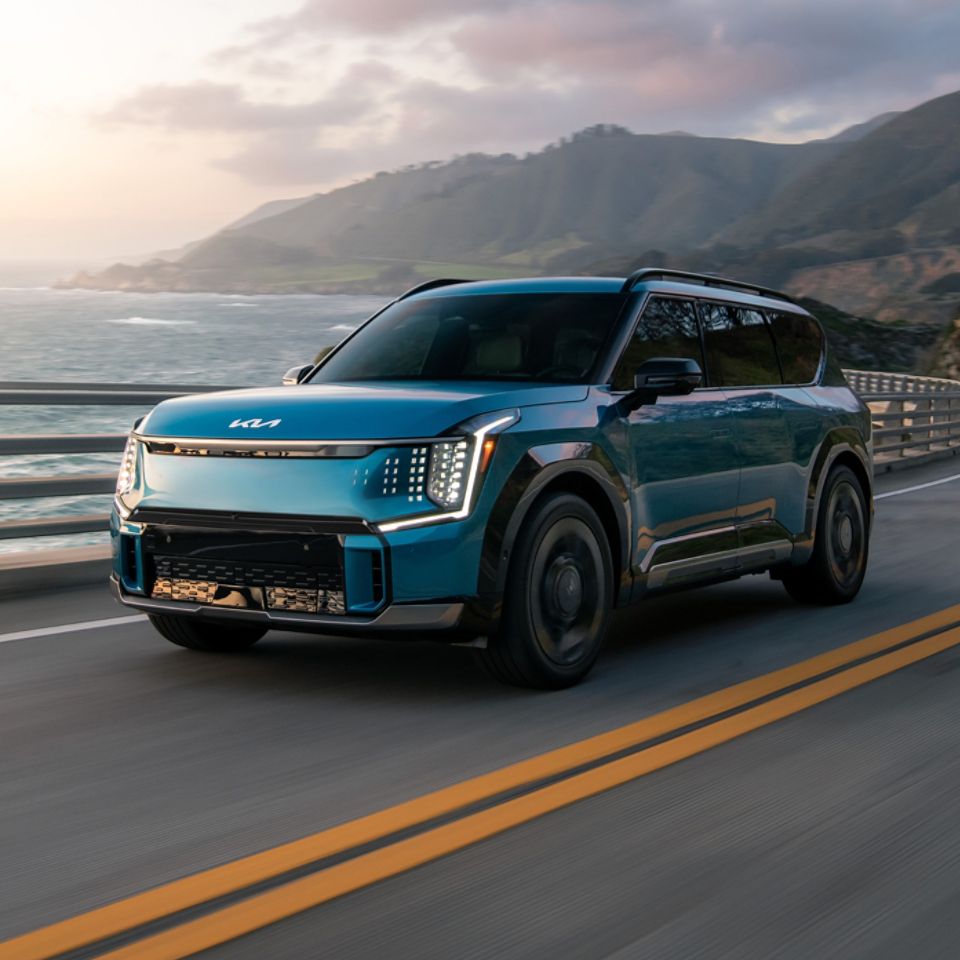 Side View of a blue 2026 Kia EV9 driving along the coastal highway