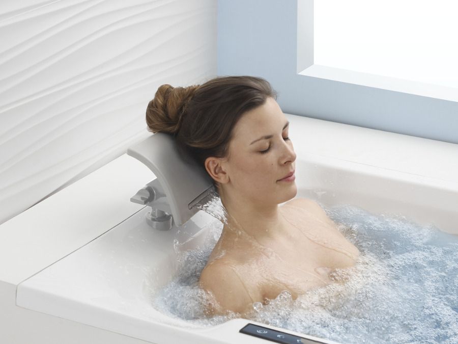 Une femme dans repose sa tête sur un coussin de tête dans une baignoire balnéo : ambiance détente 