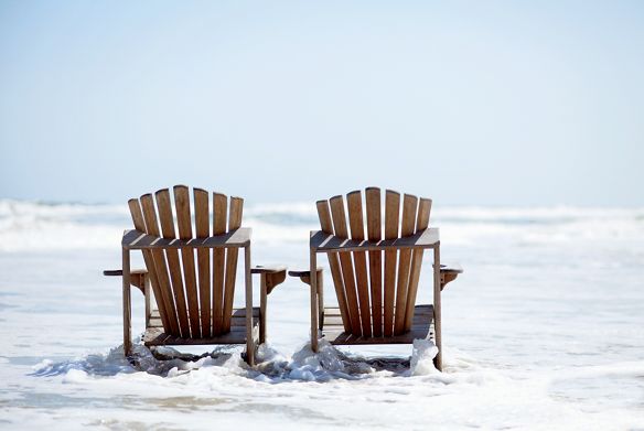 Two Adirondack chairs at the edge of the ocean