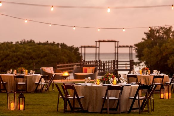 Tables and chairs and lounge seating set up on a lawn with lanterns and a walkway leading to the ocean