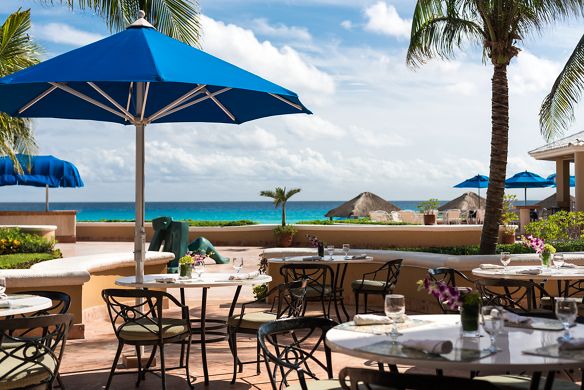 Dining tables with umbrellas sit on a patio overlooking the ocean
