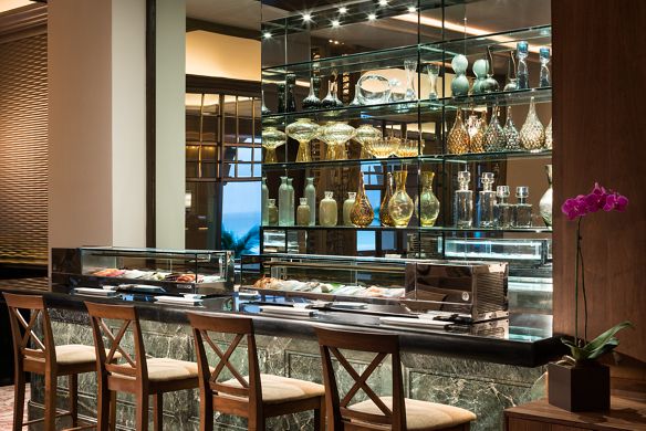 Chairs line a bar counter with glass cases filled with fresh seafood are overlooked by shelves lined with glass bottles 