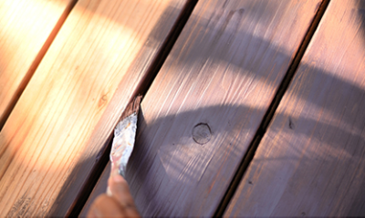 A person applying stain between deck boards with a brush.