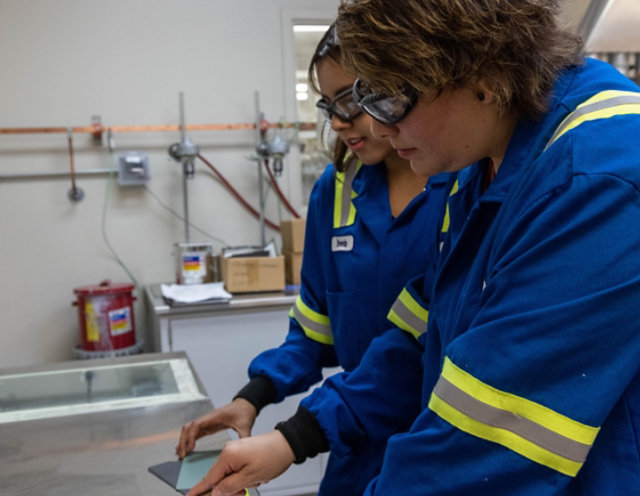 2 lab technicians in blue lab coats working on paint formulation in a lab.