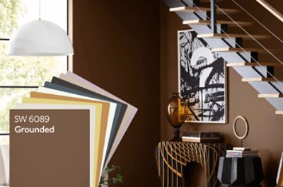 Stack of color cards featuring SW 6089 Grounded and the 2025 Color of the Year palette. A room painted in Grounded 6089 with art and a modern staircase.