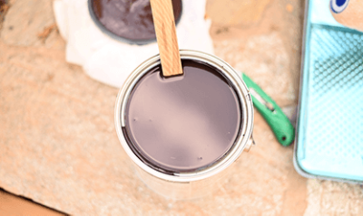A open can of dark stain with a stir stick in the can.