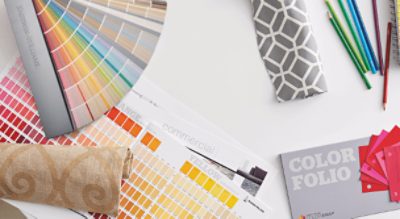 A table covered with color swatches, fan decks, fabric and colored pencils.