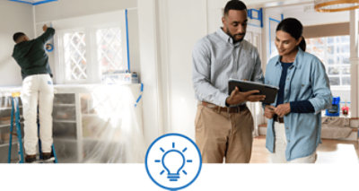 Two people looking at a tablet while a paint pro tapes off trim.